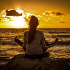 Symbolbild für Spiritualität: junge Frau meditiert vor Sonnenuntergang am Meer