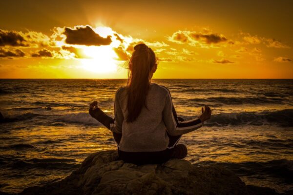 Symbolbild für Spiritualität: junge Frau meditiert vor Sonnenuntergang am Meer